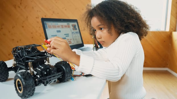 Smart african girl build robotic car while using wires while using laptop setting or writing prompt code. Skilled female student working on computer in STEM technology online classroom. Erudition.