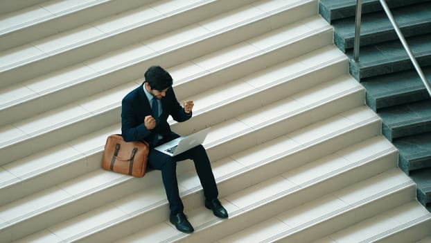 Top view business man celebrate successful project while sitting at stairs. Smart project manager getting new gob, getting promotion, increasing sales while calling friends by using laptop. Exultant.