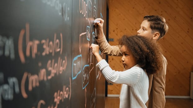 Diverse student brainstorm engineering prompt on blackboard. Group of happy children helping, support to create and design STEM technology classroom in casual cloth. Site view. Closeup. Erudition.