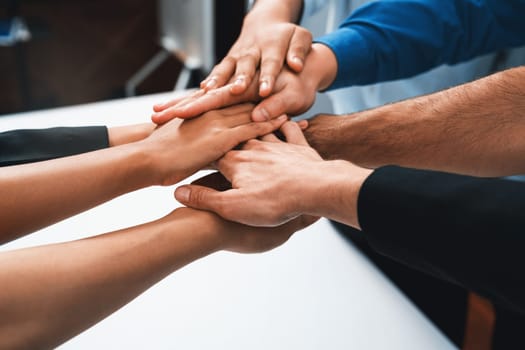 Group of diverse office worker join hand together in office room symbolize business synergy and strong productive teamwork in workplace. Cooperation and unity between business employee. Prudent