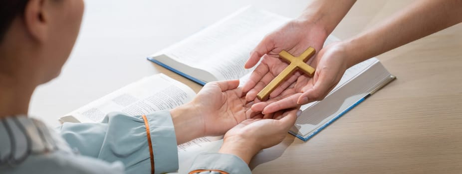 Close-up women prayer deliver holy bible book and holy cross to young believer. Spreading religion symbol. Concept of hope, religion, christianity and god blessing. Warm background. Burgeoning.