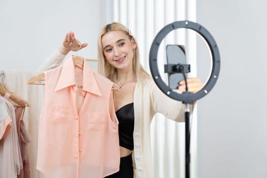 Young social medial content creator woman make fashion video. Blogger smiles to camera and light ring while making persuasive online clothing sell vlog to audience or follower. Blithe