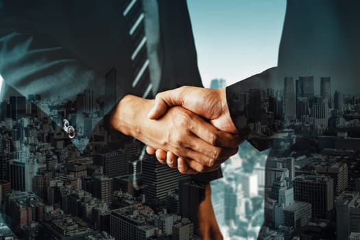 Double exposure image of business people handshake on city office building in background showing partnership success of business deal. Concept of corporate teamwork, trust partner and work agreement.