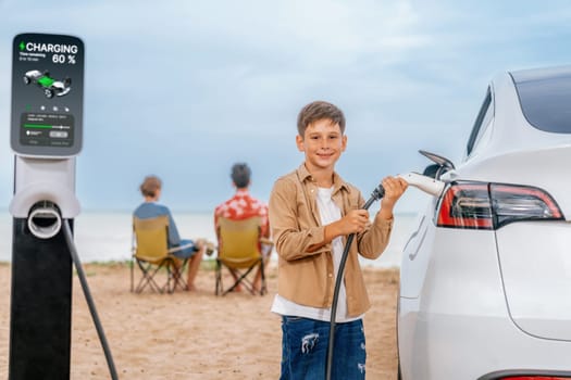 Family vacation trip traveling by the beach with electric car, little boy recharge EV car while his family enjoy seascape beach. Family trip with alternative energy and eco-friendly car. Perpetual