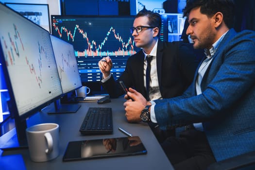 Two stock exchange traders discussing dynamic investment graph in currency rate on monitor at night. Businessman partners coffee meeting in high stock market in neon light at workplace. Sellable.