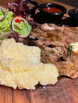 Juicy beef steak with salad and mashed potato along with pepper corn sauce served on wooden plate wooden stone table. Top view on a restaurant