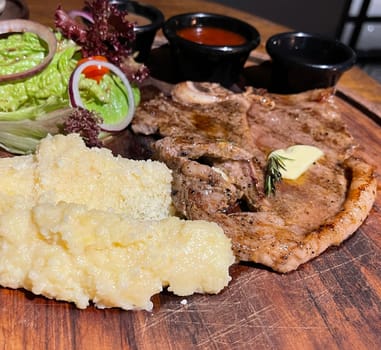 Juicy beef steak with salad and mashed potato along with pepper corn sauce served on wooden plate wooden stone table. Top view on a restaurant