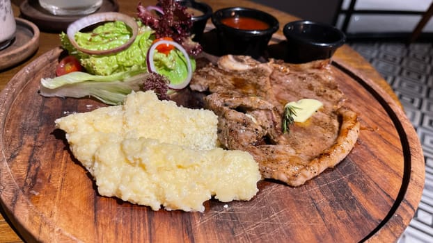 Juicy beef steak with salad and mashed potato along with pepper corn sauce served on wooden plate wooden stone table. Top view on a restaurant