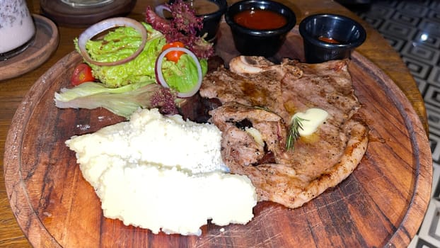 Juicy beef steak with salad and mashed potato along with pepper corn sauce served on wooden plate wooden stone table. Top view on a restaurant