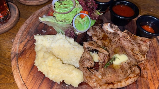 Juicy beef steak with salad and mashed potato along with pepper corn sauce served on wooden plate wooden stone table. Top view on a restaurant