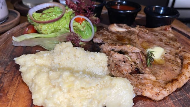Juicy beef steak with salad and mashed potato along with pepper corn sauce served on wooden plate wooden stone table. Top view on a restaurant