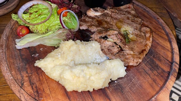 Juicy beef steak with salad and mashed potato along with pepper corn sauce served on wooden plate wooden stone table. Top view on a restaurant