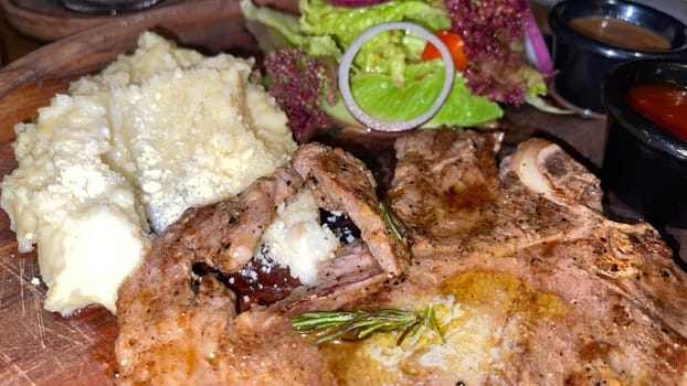 Juicy beef steak with salad and mashed potato along with pepper corn sauce served on wooden plate wooden stone table. Top view on a restaurant