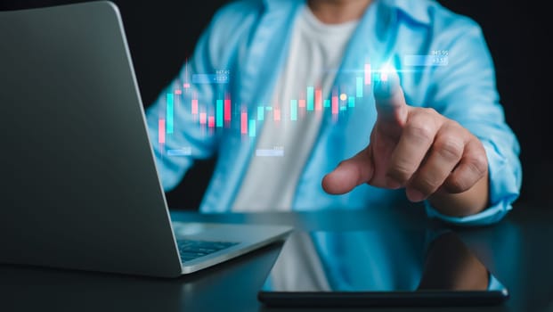 Close up of businessman hand pointing at candlestick chart on dark background. Financial crisis and recession concept, internet trading concept, business person touching chart by finger, Forex. 