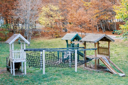 Wooden playground in the autumn forest with slides and agility mesh bridge. High quality photo