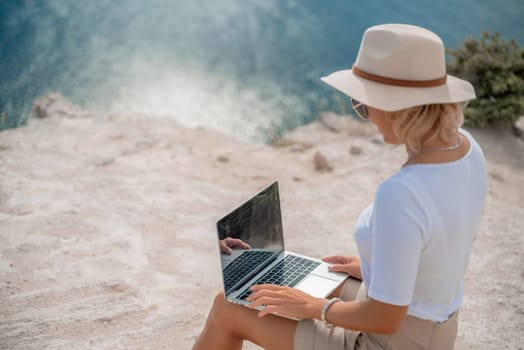 Freelance women sea working on the computer. Good looking middle aged woman typing on a laptop keyboard outdoors with a beautiful sea view. The concept of remote work