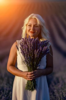 Blonde woman poses in lavender field at sunset. Happy woman in white dress holds lavender bouquet. Aromatherapy concept, lavender oil, photo session in lavender.