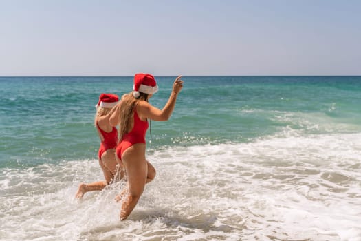 Women in Santa Claus hats run into the sea dressed in red swimsuits. Celebrating the New Year in a hot country.