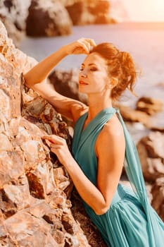 Woman green dress sea. Woman in a long mint dress posing on a beach with rocks on sunny day. Girl on the nature on blue sky background