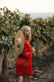 portrait of a happy woman in the summer vineyards at sunset. woman in a hat and smiling