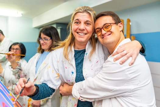 Portrait of a happy man with down syndrome embracing his painting teacher during class