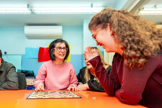 Caregiver and woman with special needs playing with board games on a table of a day center