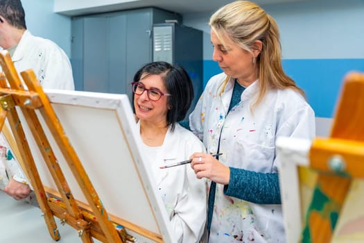 Teacher and woman with special needs in an art class painting in a canvas