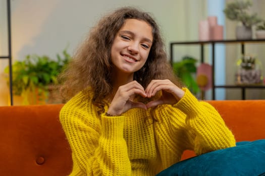 I love you. Caucasian child kid girl makes symbol of love, showing heart sign to camera, express romantic feelings, express sincere positive feelings. Charity, gratitude, donation. Female teen at home