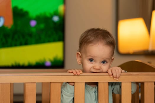 a little girl sadly gnaws the edge of her crib with her teeth while waiting for her parents.