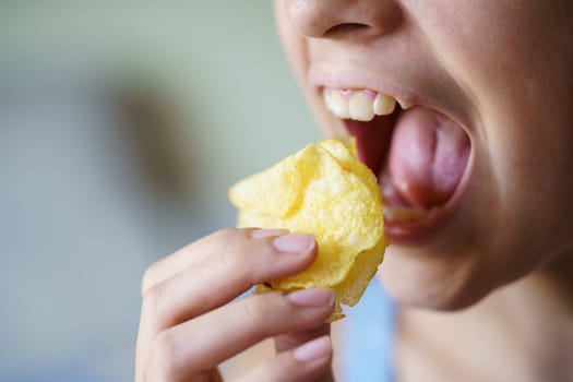 Crop anonymous young girl with mouth wide open about to eat crispy potato chips at home