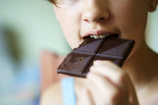 Closeup of unrecognizable teenage girl eating delicious chocolate bar at home