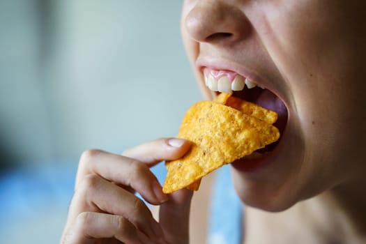 Closeup of crop anonymous teenage girl with mouth wide open about to eat spicy nacho chips at home
