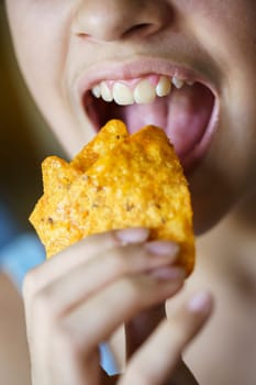 Closeup of anonymous teenage girl with mouth wide open about to eat spicy tortilla chips at home