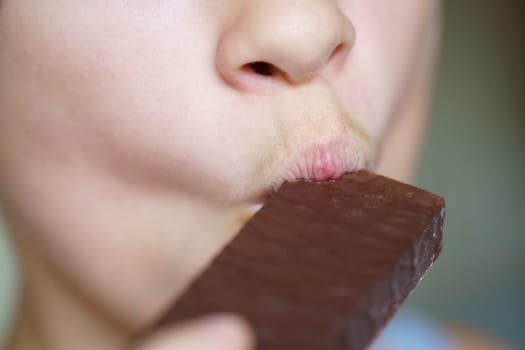 Closeup of crop unrecognizable young girl eating delicious chocolate protein bar at home