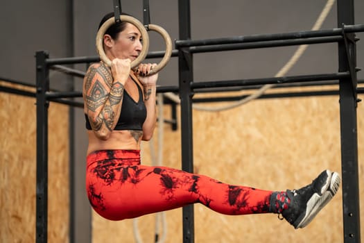 Strong mature woman hanging from olympic rings while working out in a gym