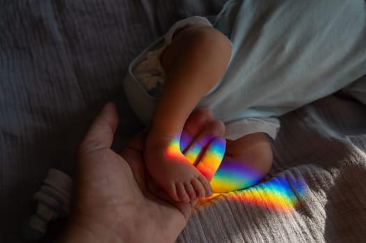 A man holds his newborn son by the leg. Beam of light through a prism