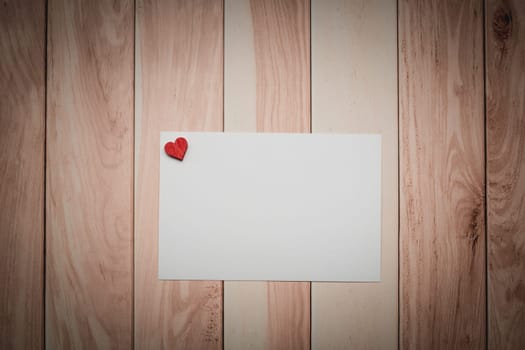 A conceptual white paper adorned with a love-themed red heart on a wooden table for Valentine's Day