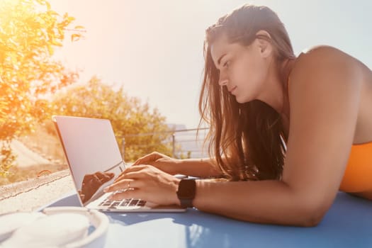 Digital nomad, Business woman working on laptop by the sea. Pretty lady typing on computer by the sea at sunset, makes a business transaction online from a distance. Freelance, remote work on vacation