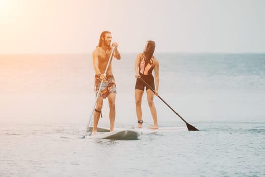 Sea woman and man on sup. Silhouette of happy young woman and man, surfing on SUP board, confident paddling through water surface. Idyllic sunset. Active lifestyle at sea or river