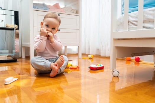 The baby holds the toy with his hands while sitting on the floor and playing with toys.