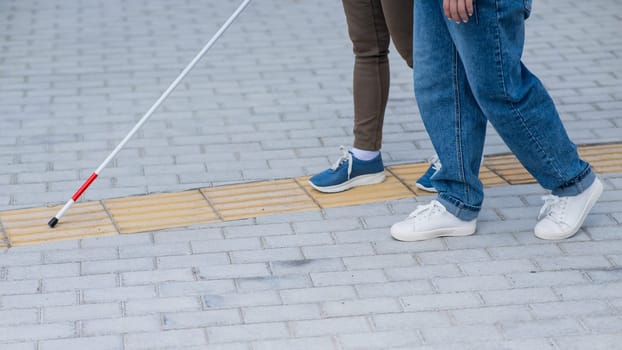 Close-up of a woman's legs accompanying a blind elderly lady outdoors