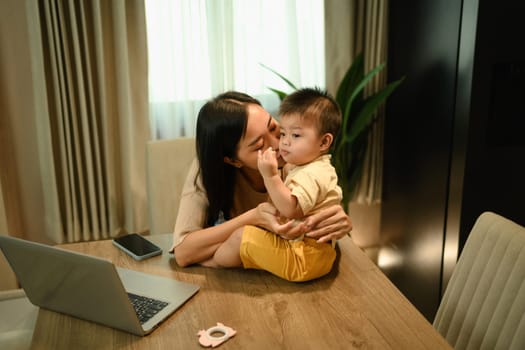 Loving Asian mother kissing her baby boy at home