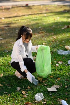 Young woman picking up litter in the public park. Environmental responsibility concept.