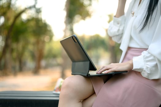 Cropped shot businesswoman sitting on wooden park bench and using digital tablet.
