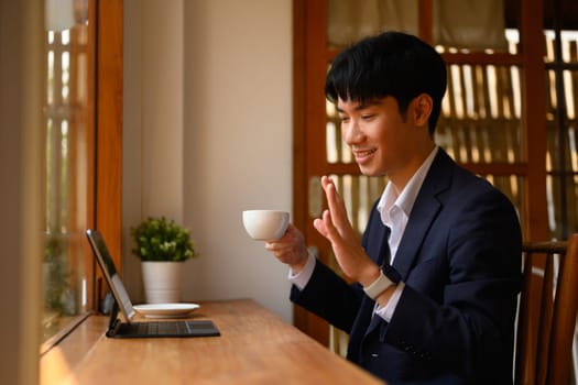 Young asian man in business suit talking on video call over digital tablet at cafe.