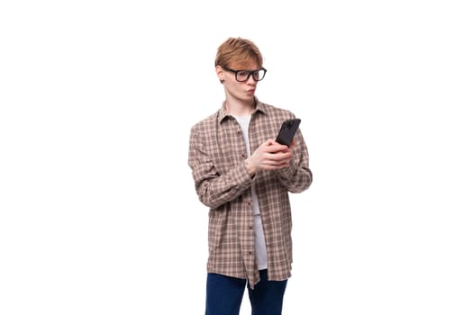 young joyful red-haired guy with glasses in a plaid shirt writes a message on the phone.