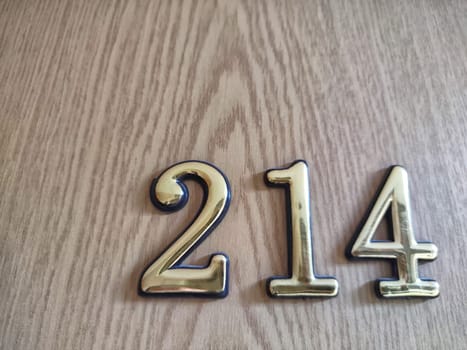 Three-dimensional brass numbers affixed to wood. Brass Numerals 214 Mounted on Wooden Surface. Background