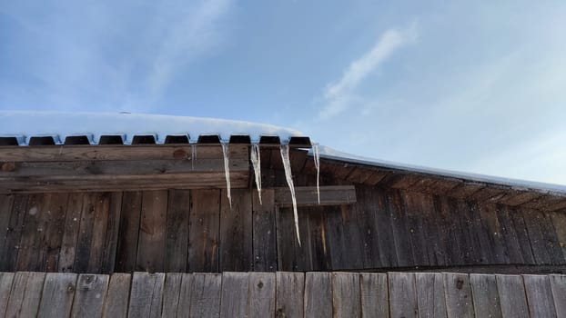 Sharp icicles from melted snow hanging from eaves of roof. Beautiful transparent icicles. Icicles on eaves of the house