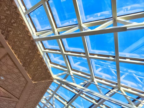 An ornate ceiling pattern under clear blue sky through a glass rooftop. Intricate Ceiling Design and Glass Roof in a Modern Structure
