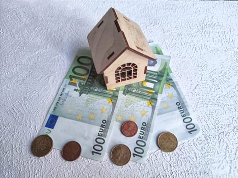 Miniature house placed atop European currency, indicating real estate investment or savings. Wooden Miniature House on Euro Banknotes and Coins